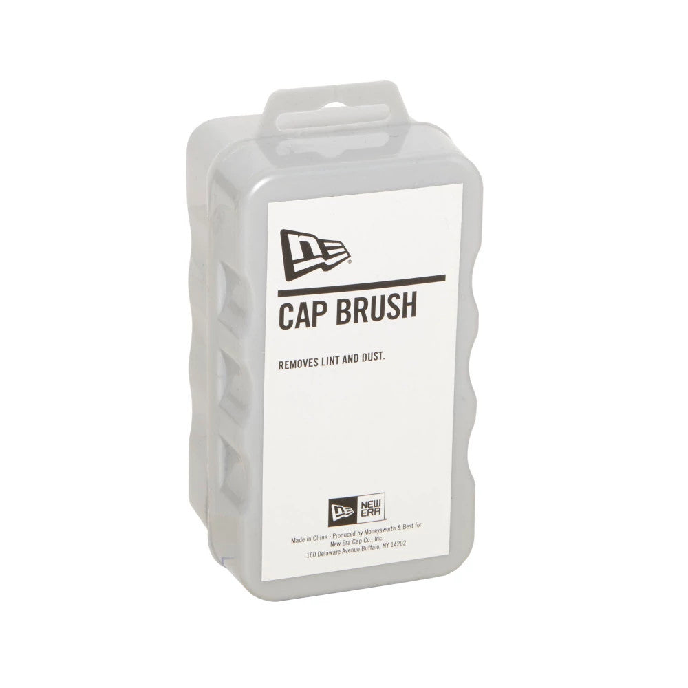 New Era Cap Brush, three-quarter view showing the packaging with New Era logo at the top, bold "Cap Brush" text and smaller print stating “Removes Lint and Dust” on the front, with a clear plastic cover.