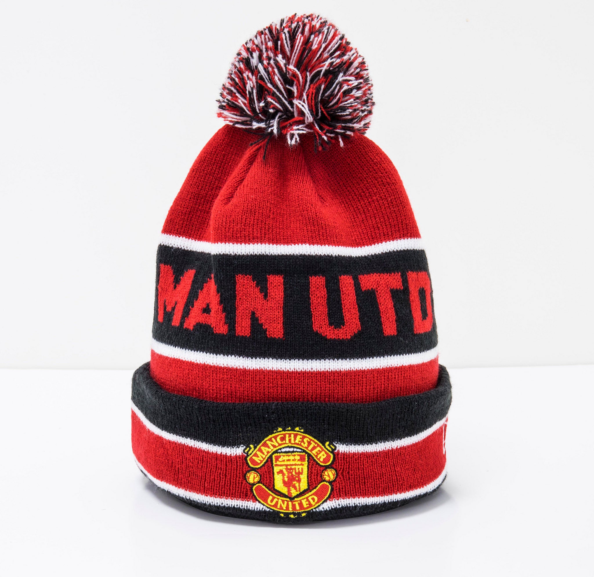 Manchester United Striped Red Multi Bobble Beanie Hat, front view showing a red, black, and white pom-pom on top, with “Man Utd” lettering on the crown and a Manchester United crest patch on the cuff.