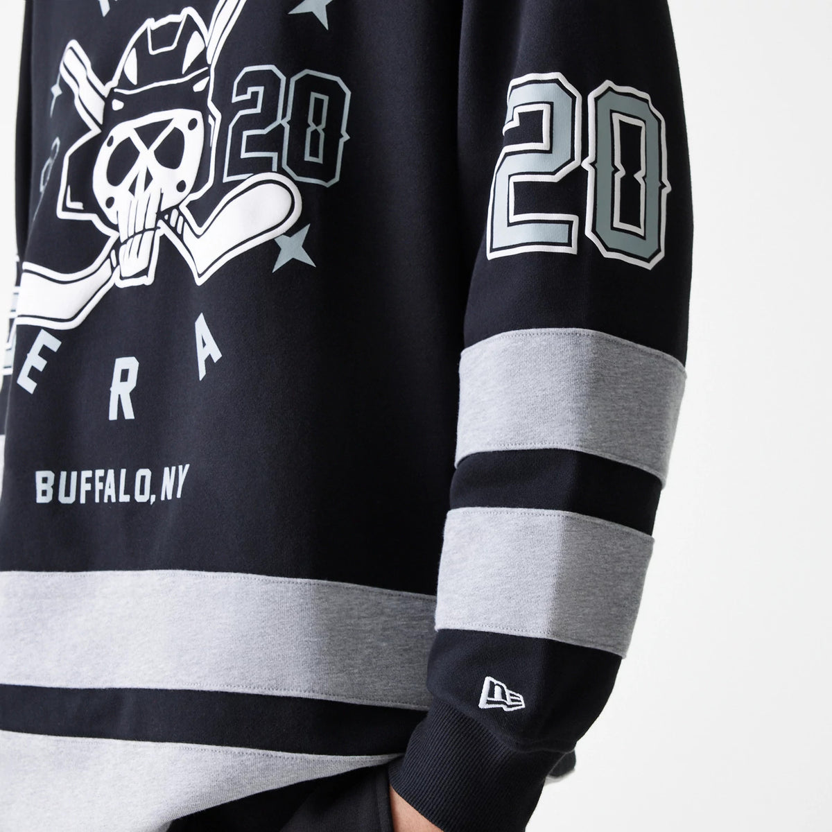 New Era Street Dangle Grey Pullover Hoodie, side view showing the arm with grey and black striped design, a raised New Era logo on the cuff, and a large graphic print of hockey sticks and skull on the chest.