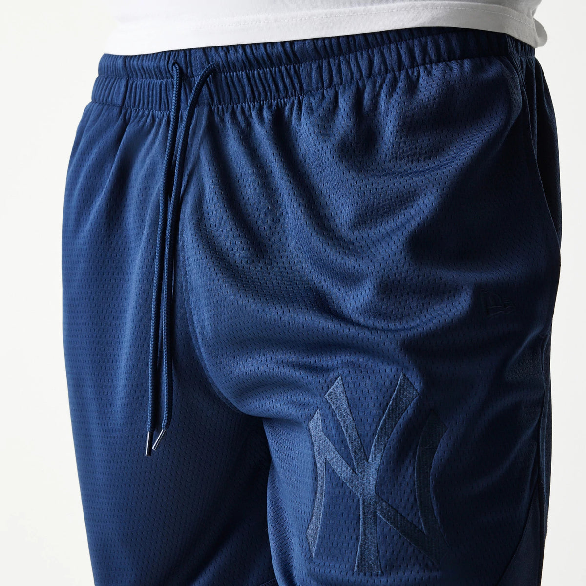 New York Yankees Tonal Pack Blue Shorts, side view showing the elastic waistband with drawstring, a debossed New York Yankees logo on the lower left leg, and a small debossed New Era logo near the pocket.