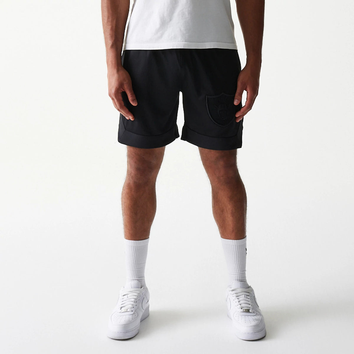 Las Vegas Raiders Tonal Pack Black Shorts, on-model view showing the black shorts with a raised Raiders logo on the left thigh, hemmed legs, and subtle detailing, paired with white socks and trainers.