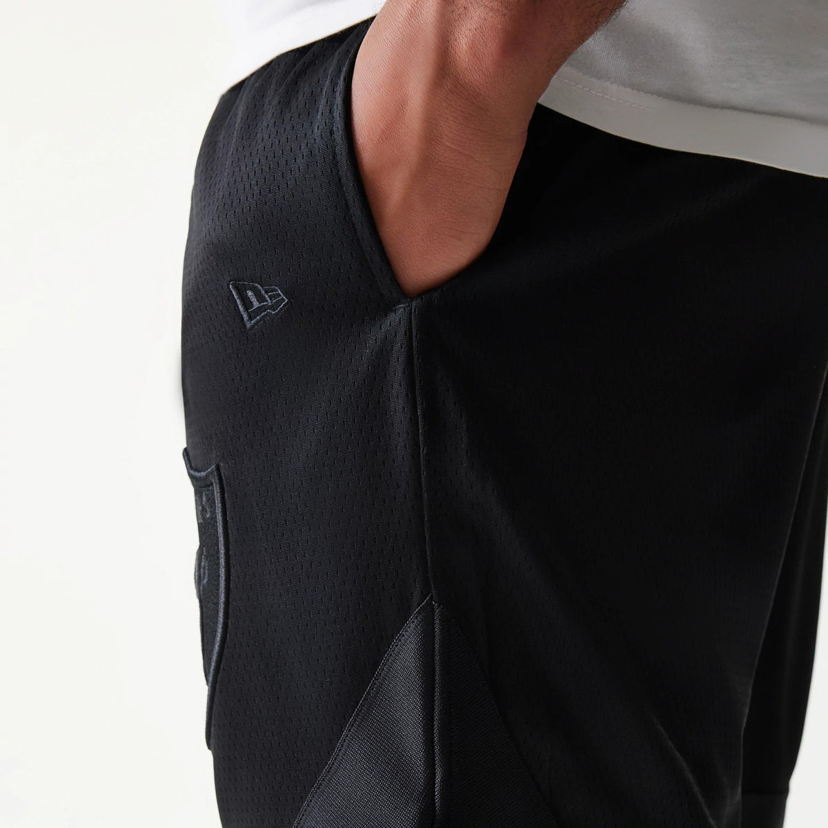 Las Vegas Raiders Tonal Pack Black Shorts, side view showing a hand in the pocket, a raised New Era logo near the pocket and the subtle shape of the Las Vegas Raiders shield below.