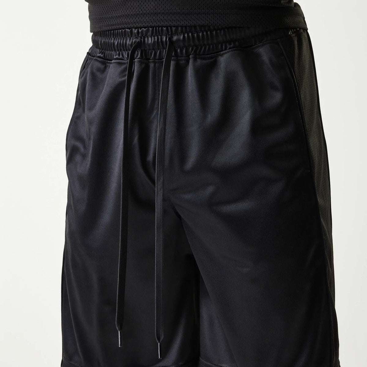New Era Retro Sports Black Mesh Shorts, front view showing black mesh fabric with an elastic waistband and drawstrings, with smooth side panels running down the length of the shorts.