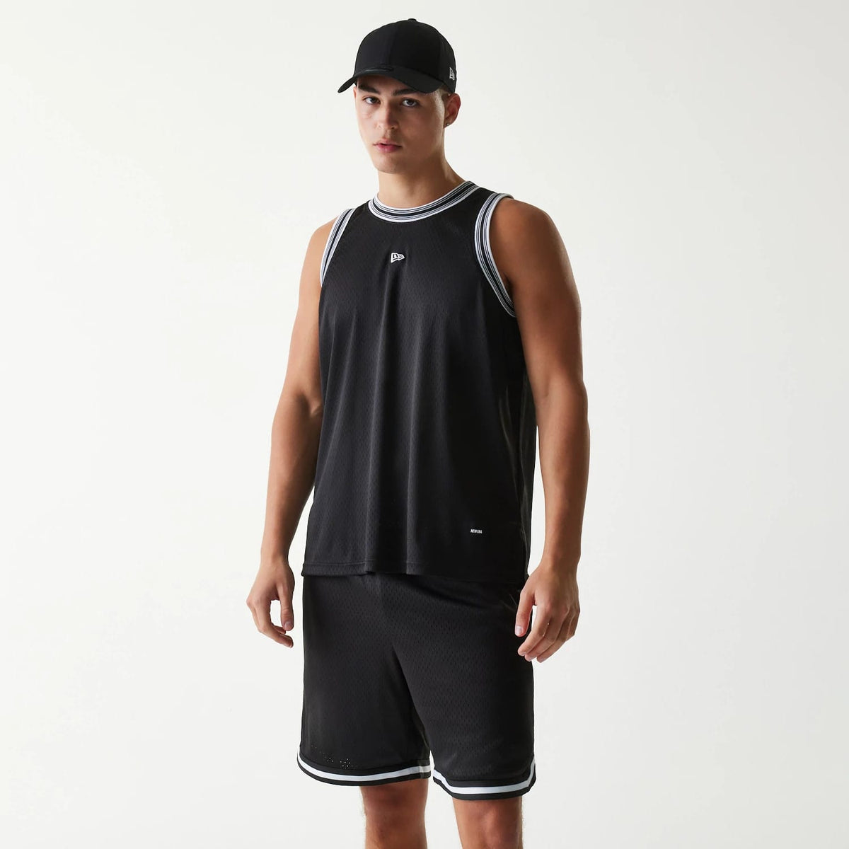 New Era Japan Mesh Black Sleeveless T-Shirt, on-model view showing the black sleeveless design with a debossed New Era logo on the left chest, white trim around the neckline and sleeves, paired with matching shorts and a black cap.