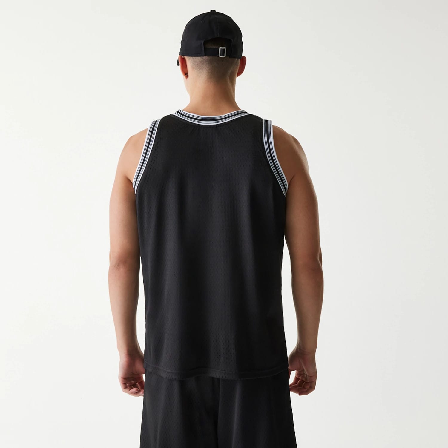 New Era Japan Mesh Black Sleeveless T-Shirt, on-model rear view showing the black mesh fabric with white trim on the shoulders and neck, paired with black shorts and a black cap featuring a debossed logo on the back.
