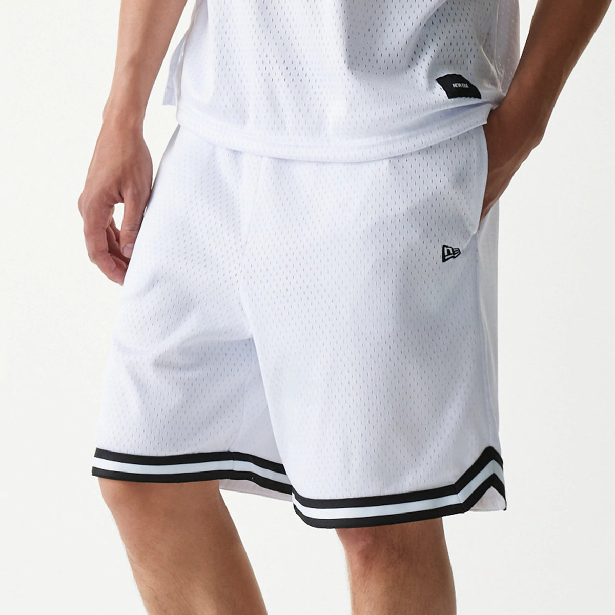 New Era Japan Mesh White Shorts, front view showing white shorts with black striped trim at the hem, a raised New Era logo on the left thigh, and a small black tag near the waistband.