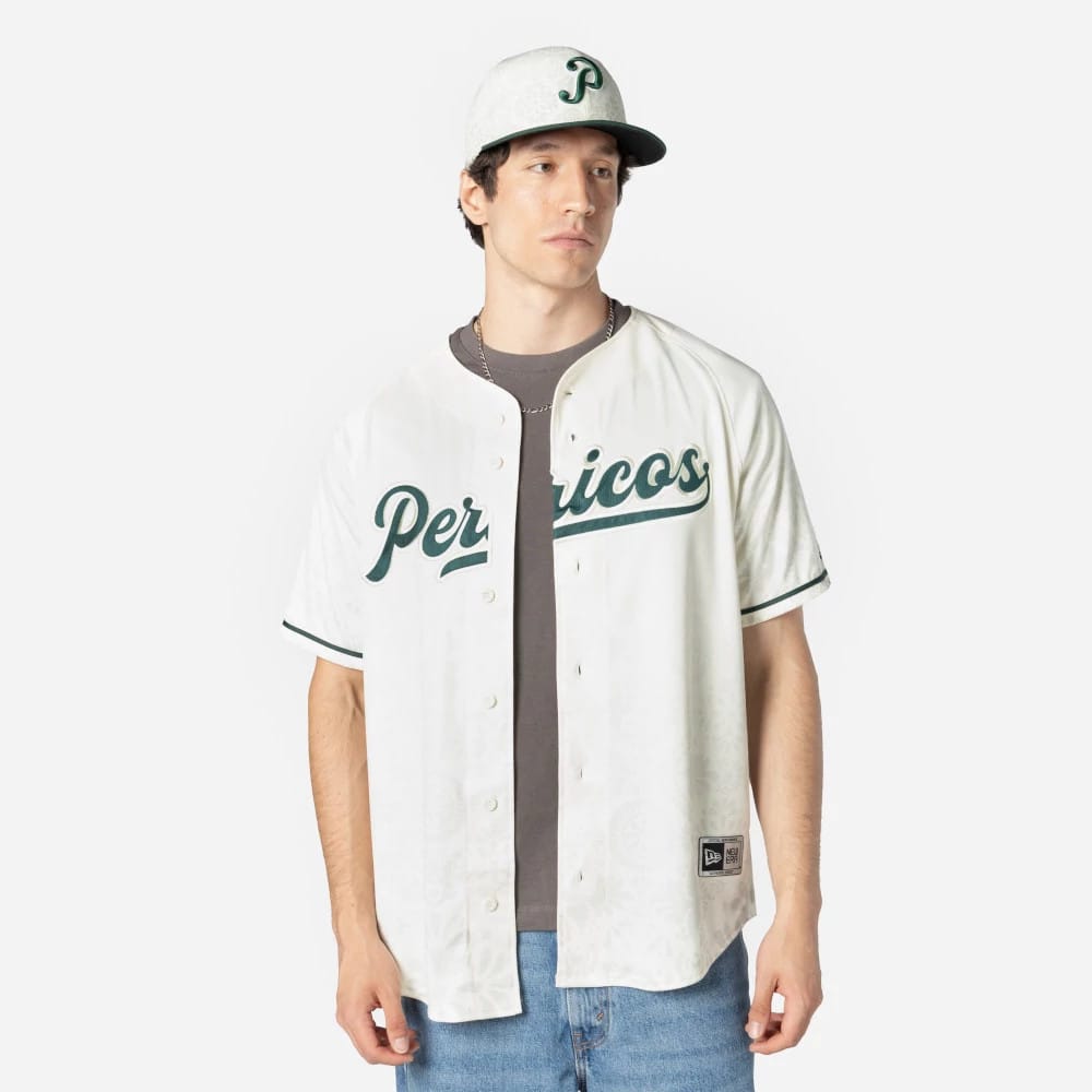Puebla Pericos Mexico LMB On Field White On-Field Jersey, on-model view with an embroidered Pericos script across the chest, paired with a matching cap featuring a green P logo, worn over a grey t-shirt and blue jeans.