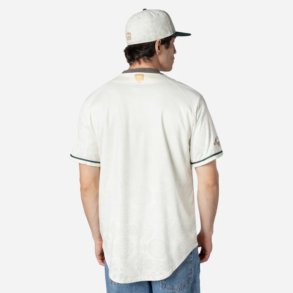 Puebla Pericos Mexico LMB On Field White On-Field Jersey, back view on a model wearing a matching white cap with green visor, featuring a gold LMB 100 logo below the neckline and subtle green trim on the sleeves.