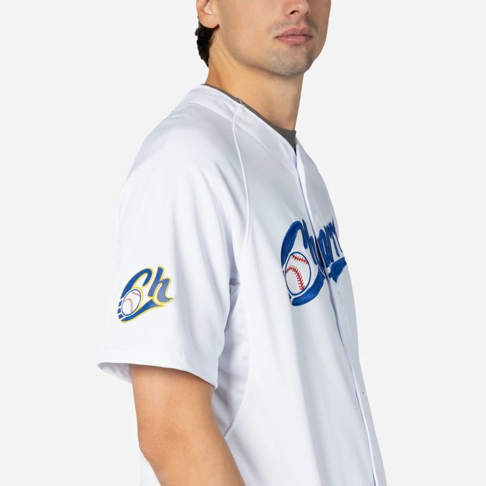 Charros De Jalisco Mexico LMB On Field White On-Field Jersey, side view on a model showing the embroidered blue Charros script logo across the chest and a detailed "Ch" baseball emblem on the sleeve.