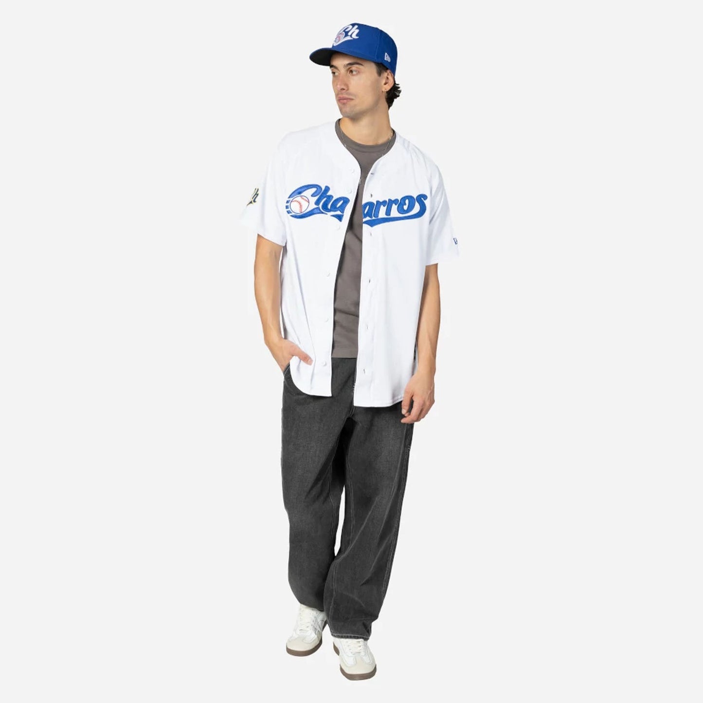 Charros De Jalisco Mexico LMB On Field White On-Field Jersey, on-model view showing the blue Charros script across the chest paired with a blue cap, highlighting the casual and relaxed fit with black trousers.