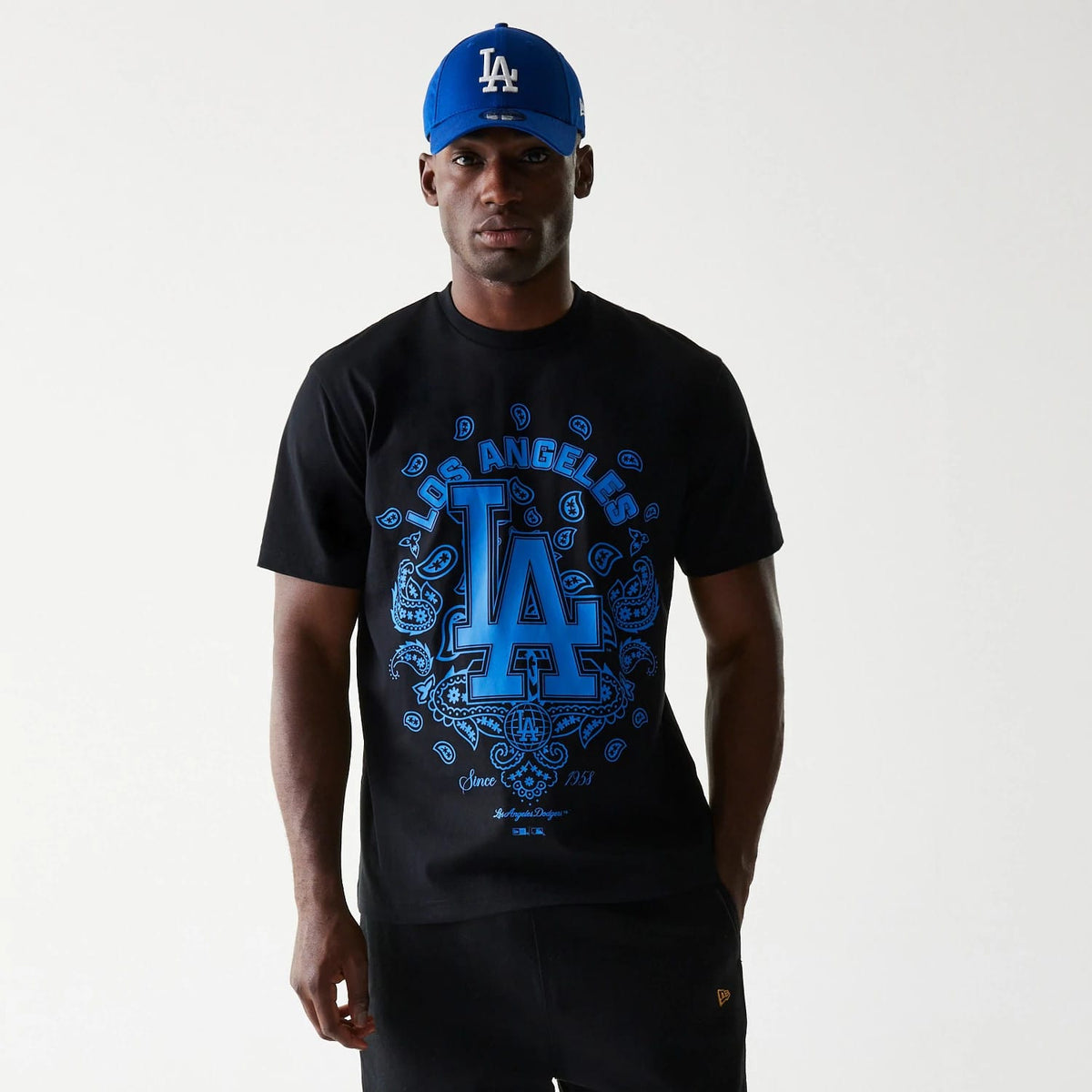 LA Dodgers MLB Paisley Black Oversized T-Shirt, on-model view showing a black t-shirt with a large blue LA Dodgers logo and paisley design on the front, complemented by a blue cap featuring a raised white LA logo.