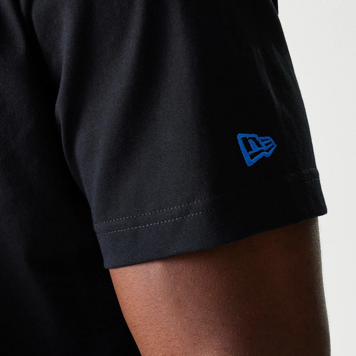 LA Dodgers MLB Paisley Black Oversized T-Shirt, side view showing the black fabric with a blue embroidered New Era logo on the sleeve edge, highlighting the simple stitching detail of the short sleeve hem.