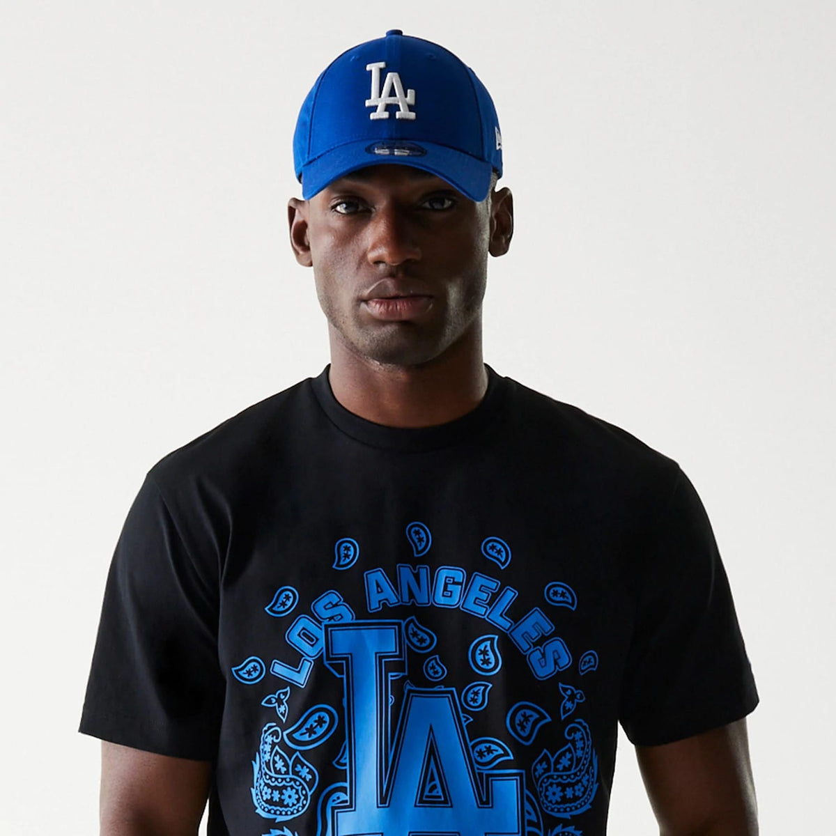 LA Dodgers MLB Paisley Black Oversized T-Shirt, on-model view showing a black t-shirt with blue paisley and LA Dodgers logo print on the front, paired with a blue cap featuring a raised white LA logo on the crown.