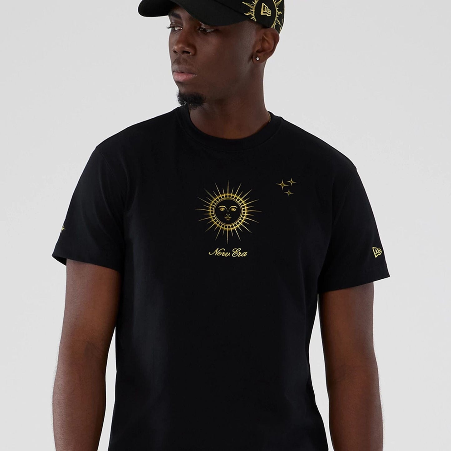 New Era Cosmic Craft Black T-Shirt, front view showing a gold printed sun design with a debossed New Era logo beneath on the chest, gold stars on the right side, and a matching logo on the left sleeve.