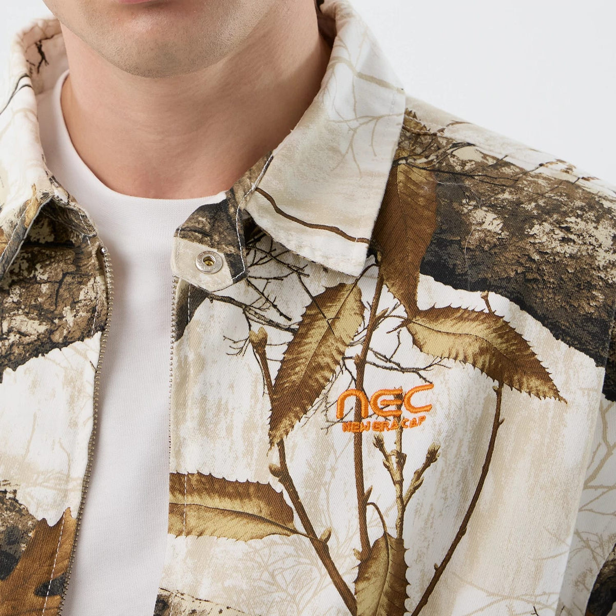 New Era Earthy Skin Real Tree Snow Jacket, front view showing the intricate brown and white tree pattern, with an orange embroidered logo on the left chest and a button closure down the middle.