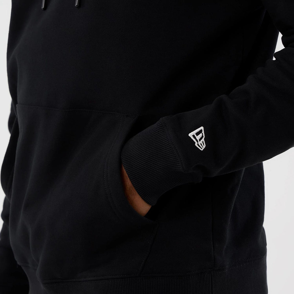 New Era Street Graphic Black Pullover Hoodie, side view showing a black hoodie with a raised white New Era logo on the lower sleeve, a wrist cuff and a hand tucked into the front pocket.