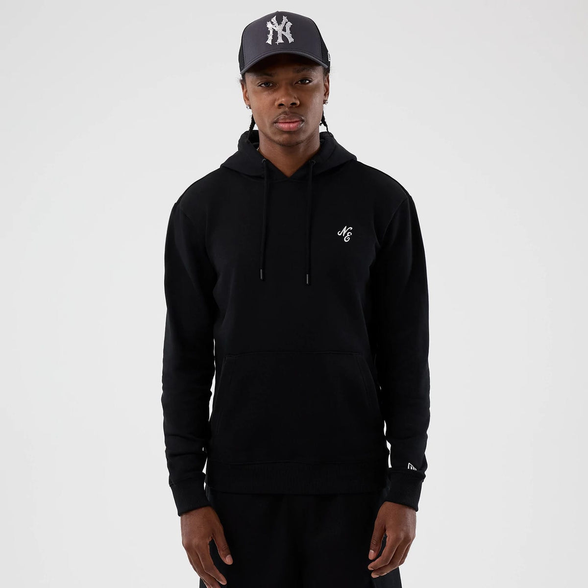 New Era Street Graphic Black Pullover Hoodie, front view showing the black hoodie worn with the NC logo embroidered on the left chest, adjustable drawstrings and a kangaroo pocket, paired with a dark cap featuring a raised NY logo.