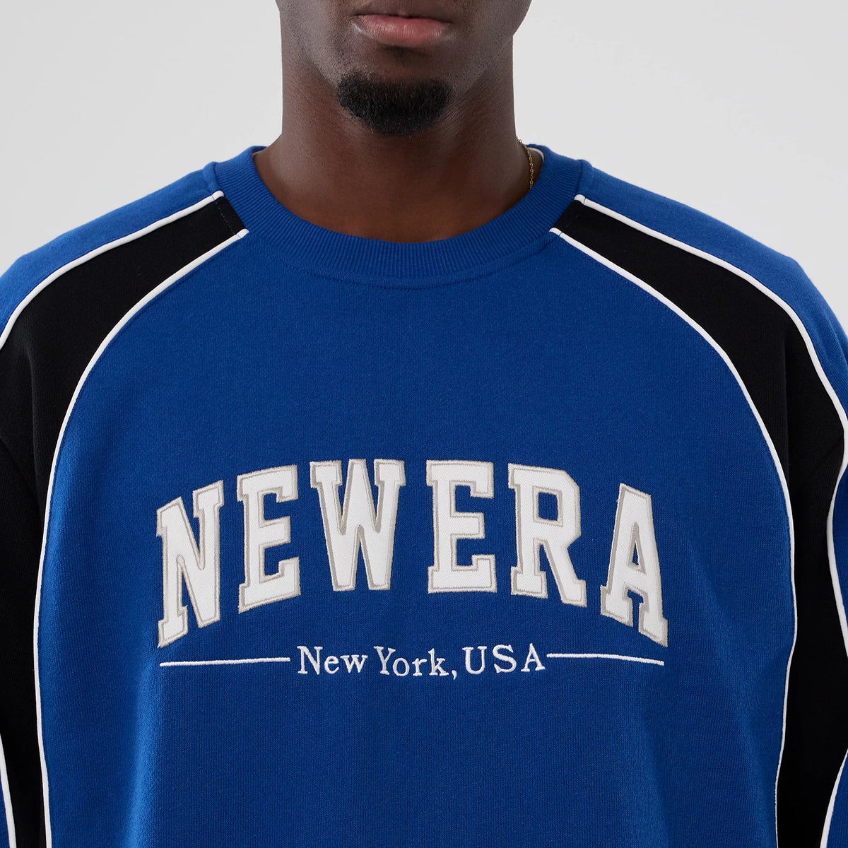 New Era Colour Block Navy Crew Neck Sweater, front view on a model showing raised grey and white NEWERA lettering across the chest, featuring black panels and white piping along the shoulders.