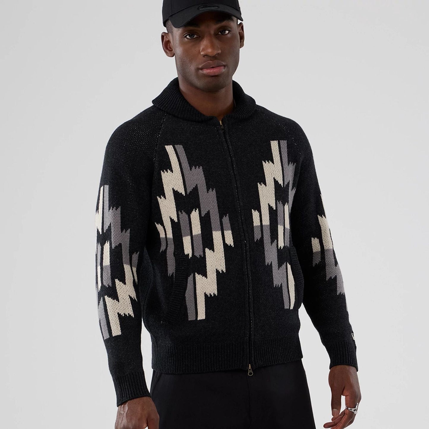 New Era Organic Cowichan Black Cardigan, three-quarter view on a model wearing a black cap, showing intricate cream and grey patterning on the front and sleeves, with a ribbed collar and zipped front.