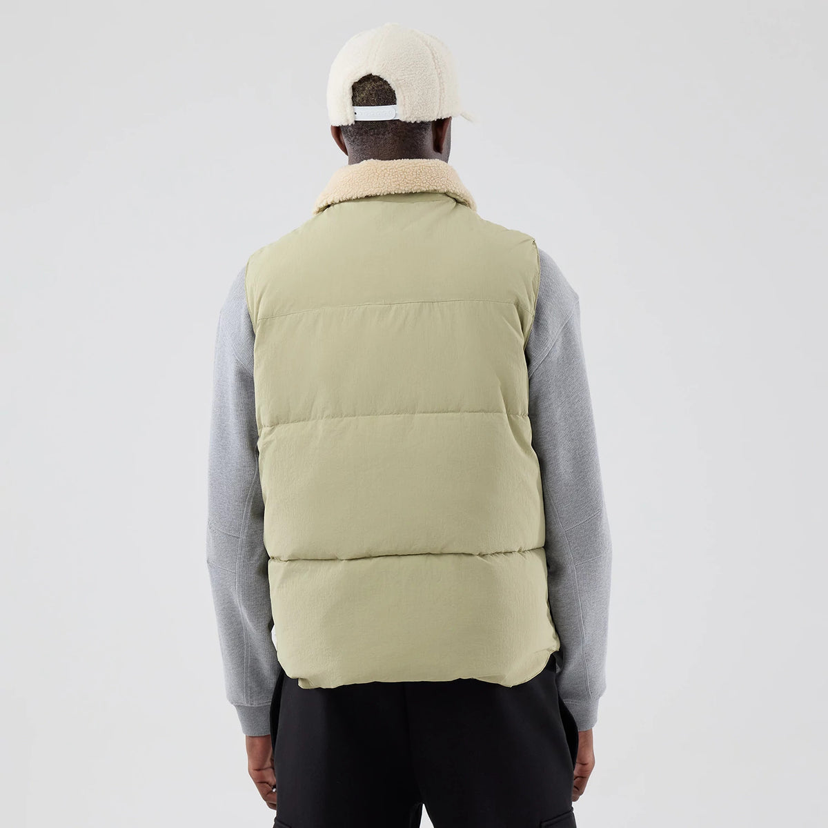 New Era Organic Boa Neck Khaki Gilet, back view on a model in a light grey sweatshirt and black trousers, showcasing the padded khaki design with a plush beige collar for added comfort and style.
