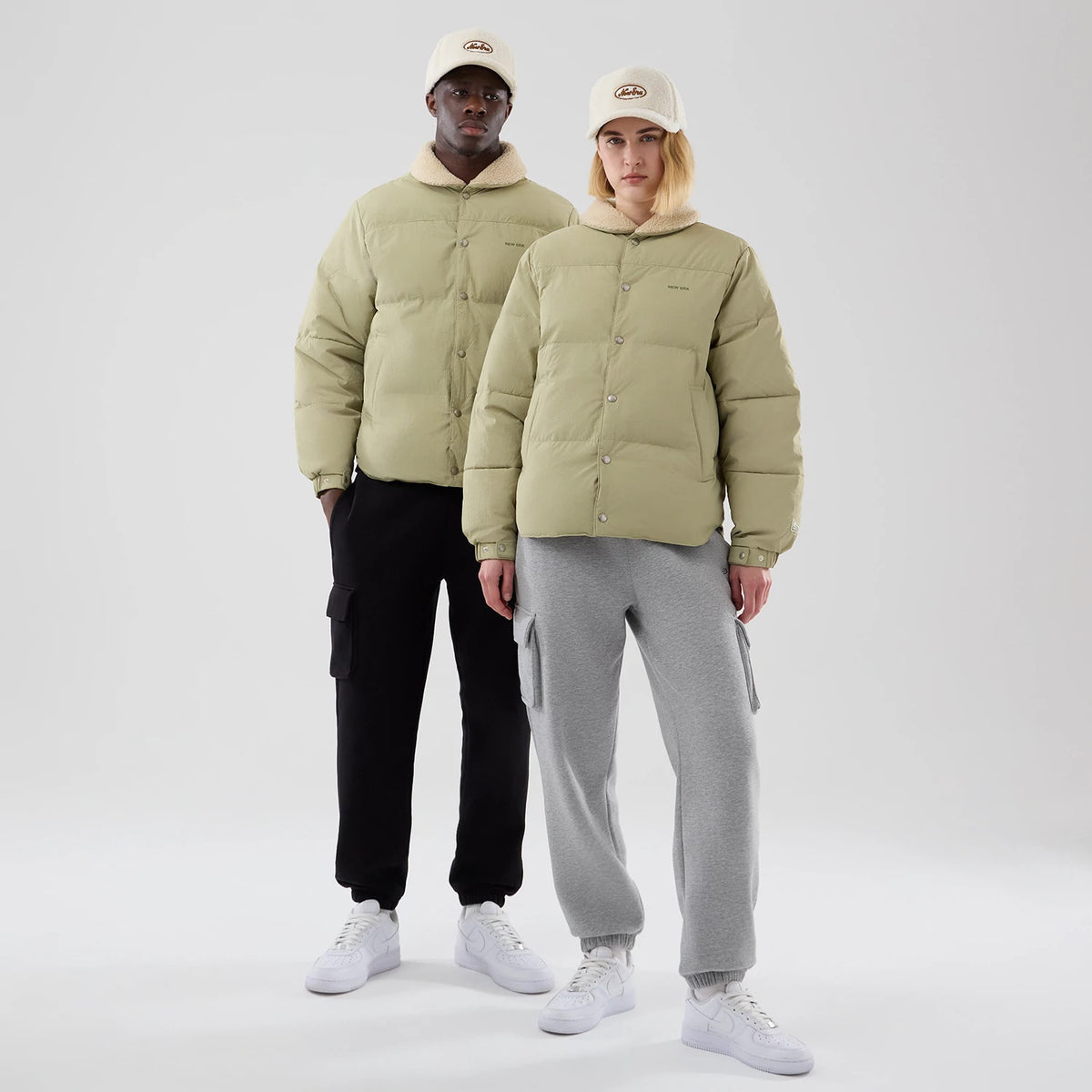 New Era Organic Boa Neck Khaki Jacket, front view showing two models wearing the khaki jackets with button closures and a raised New Era logo on the left chest, complemented by caps featuring an embossed logo.