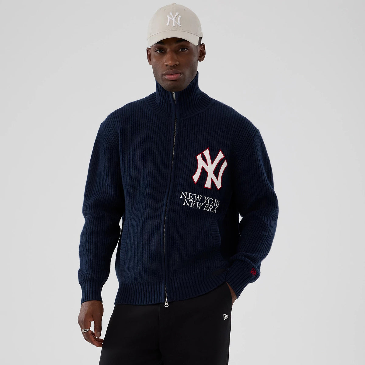 new york yankees mlb navy cardigan, on-model view showing the model in a beige cap with a white NY logo, wearing a navy zip-up cardigan featuring a large white and red NY logo and New York New Era lettering on the chest