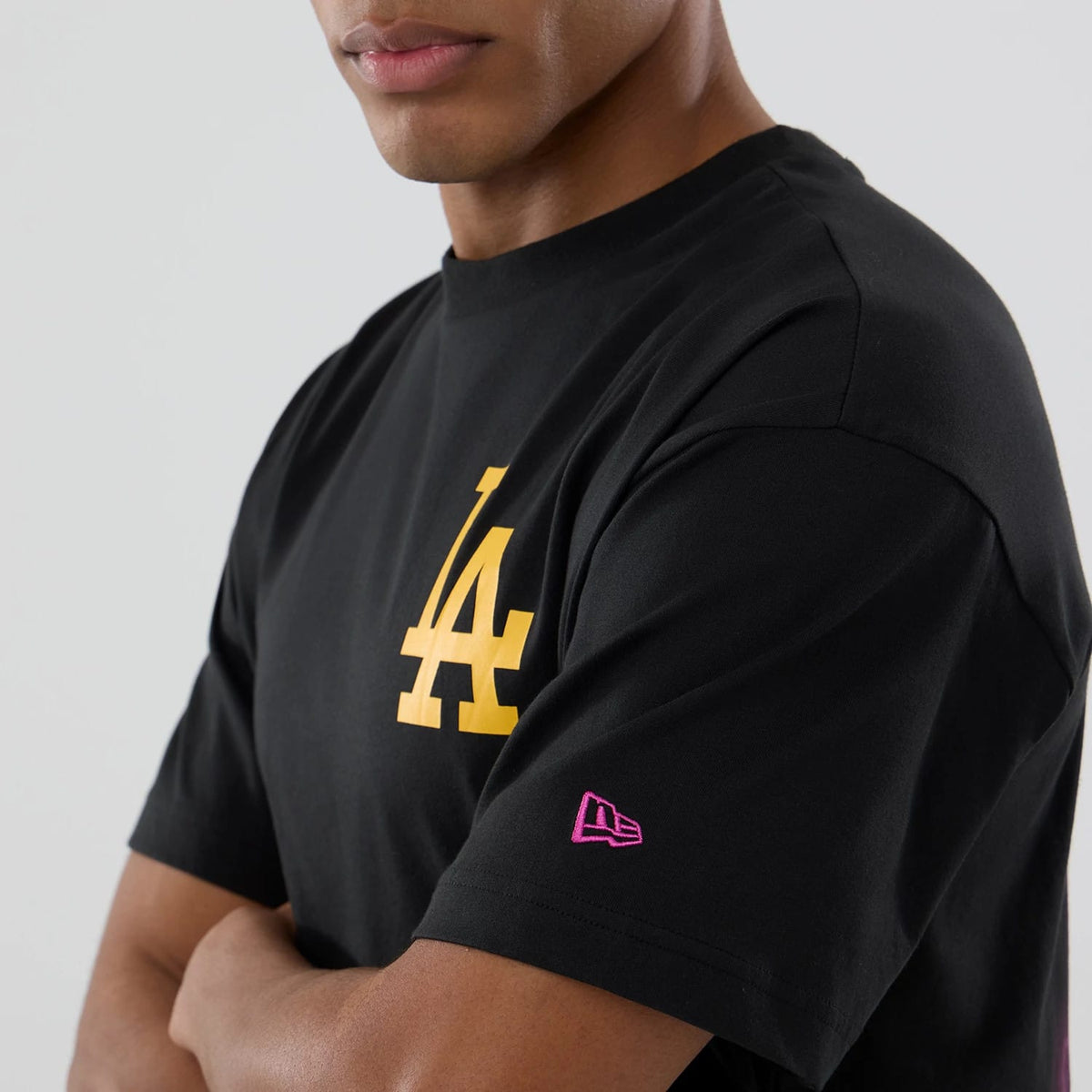 New Era LA Dodgers MLB Neon Light Black T-Shirt, side view showing the large yellow LA logo centred on the chest and a pink embroidered New Era logo on the left sleeve against the black fabric.