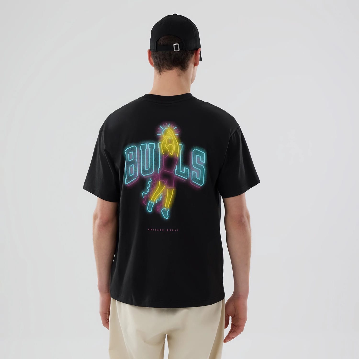 Chicago Bulls NBA Neon Light Black T-Shirt, on-model rear view showing a neon design of a basketball player in yellow and purple with the word "BULLS" in blue and neon lights effect across the back, on a black base.