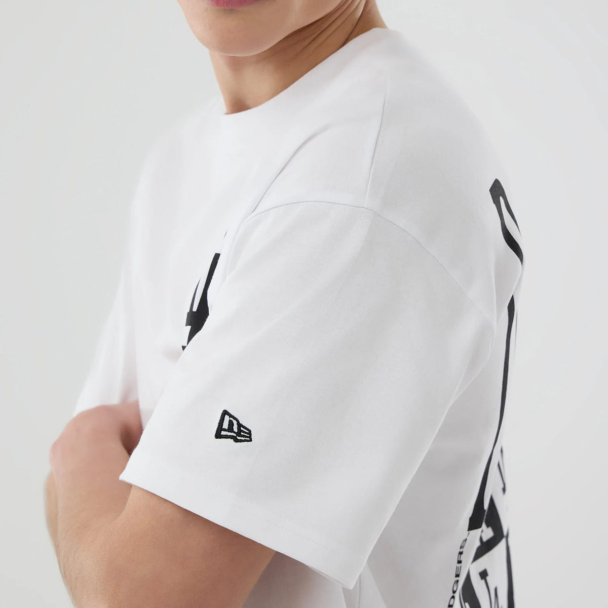 LA Dodgers MLB White T-Shirt, side view showing the clean white fabric with a black New Era logo embroidered on the sleeve and partial black graphic design extending from the back to the side.