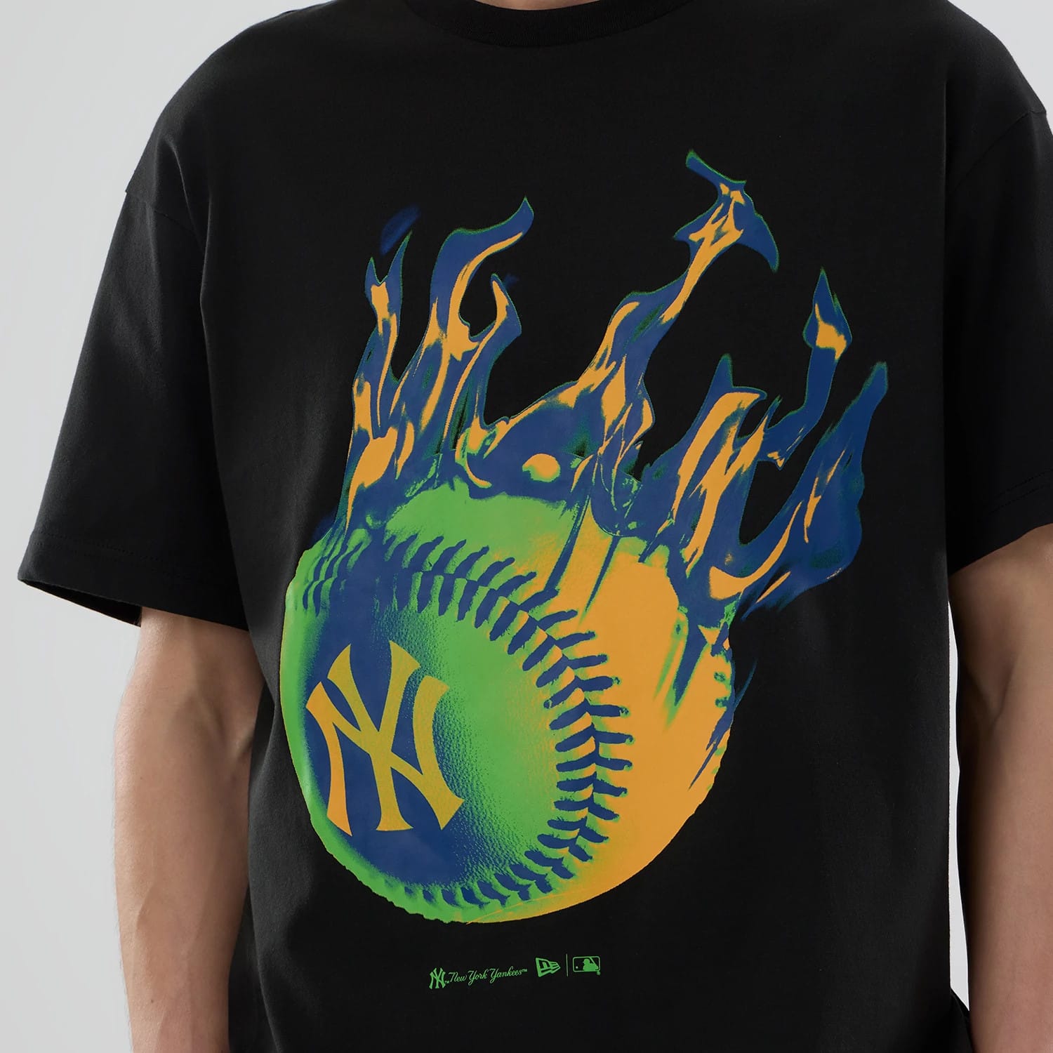 New York Yankees MLB On Fire Black Oversized T-Shirt, front view showing a vibrant graphic of a flaming baseball with a green and blue design, a yellow NY logo in the centre, on a black fabric background.