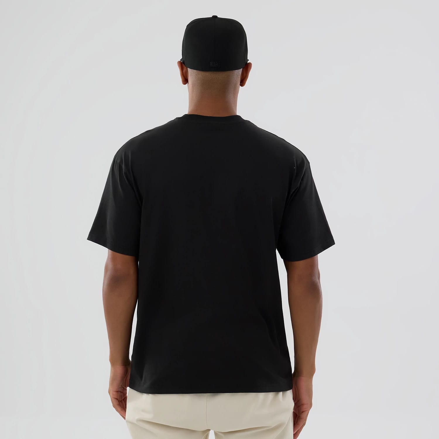 LA Dodgers MLB On Fire Black Oversized T-Shirt, rear view showing a plain black T-shirt with short sleeves and a relaxed fit, worn by a person with a black cap featuring a debossed logo centred at the back.