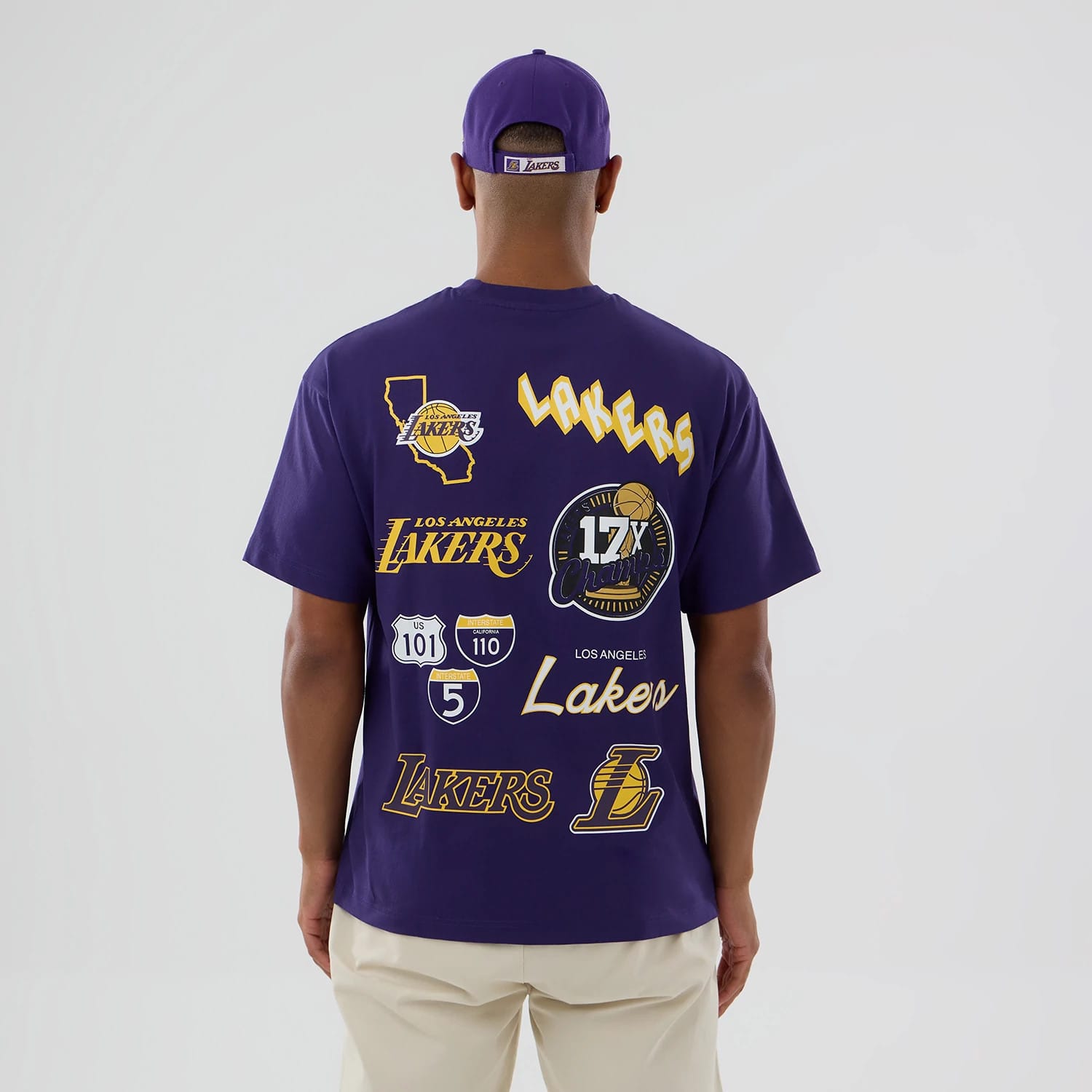 LA Lakers NBA logo Purple T-Shirt, rear view showing a series of Lakers-themed graphics including the team name, a map outline, and a 17X Champions emblem, with a man wearing a matching purple cap.