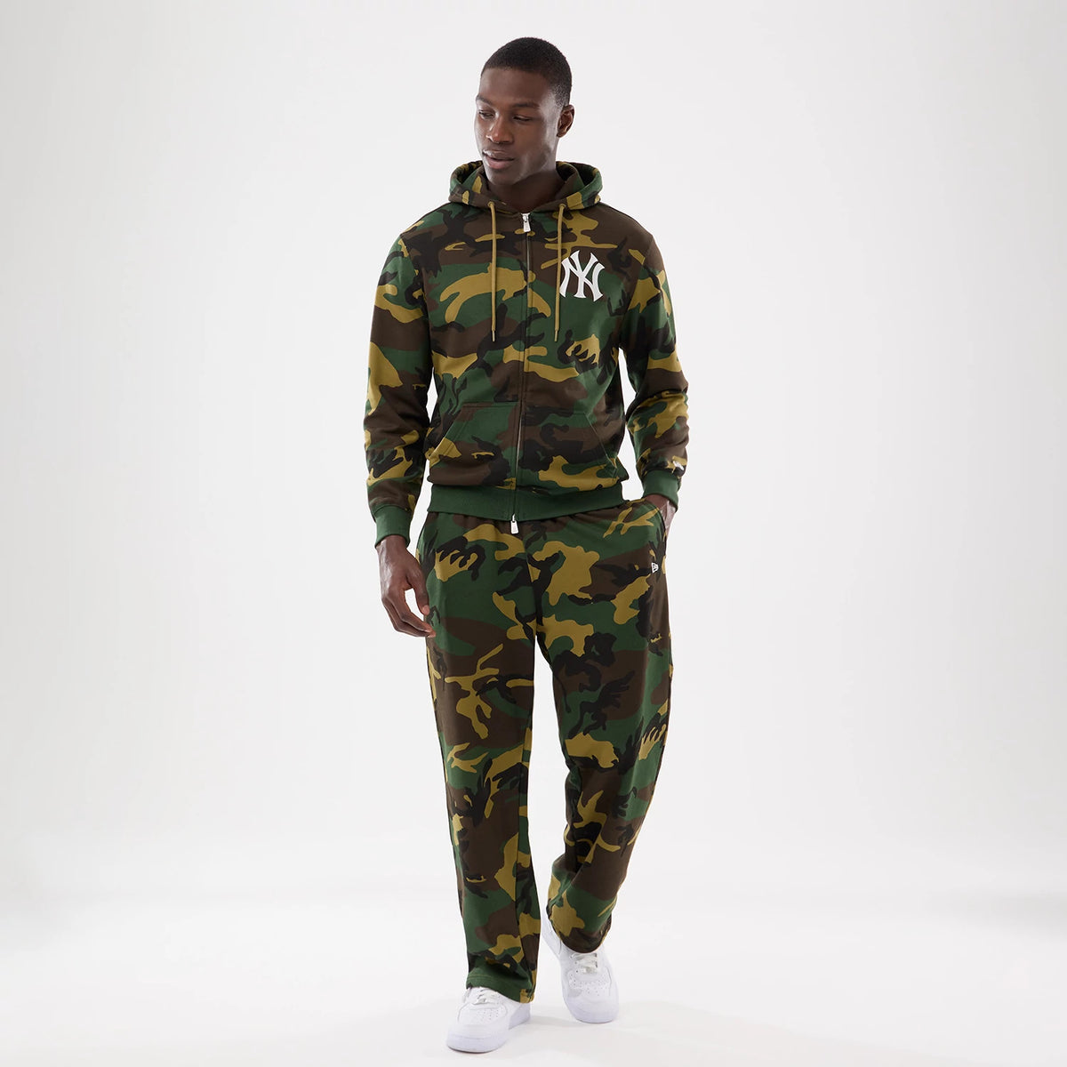 New Era Woodland Camo Joggers, on-model showing a relaxed fit with all-over camouflage pattern, paired with a matching hoodie featuring an NY logo, highlighting the cohesive streetwear look and white sneakers.