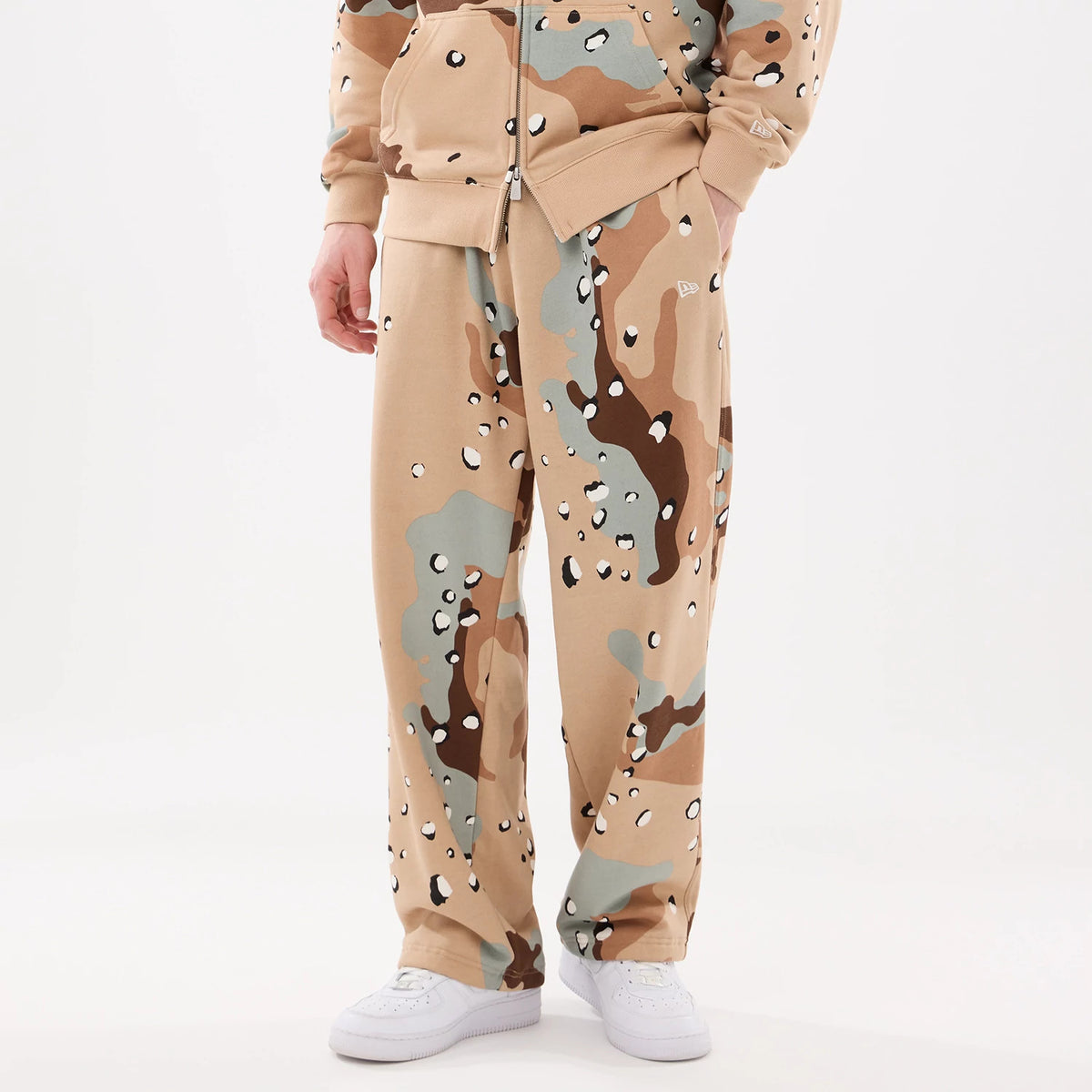 New Era Desert Camo Joggers, front view on a model wearing white trainers and a matching zipped hoodie, showing an all-over desert camouflage pattern with the New Era flag logo on the left leg.