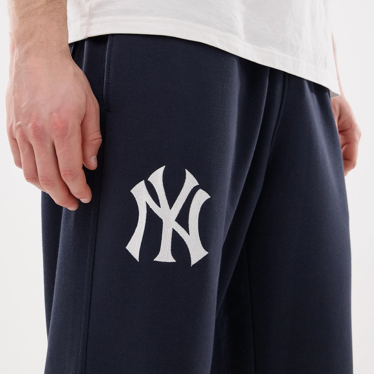 New York Yankees MLB Comfort Blue Joggers, close-up view on a model showing the white embroidered NY logo on the left thigh, paired with a plain white T-shirt, highlighting the joggers' casual fit and soft fabric.