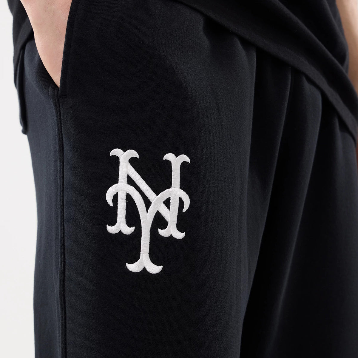 New York Mets MLB Comfort Black Joggers, side view showing the white embroidered NY logo on the upper thigh, with hands in the side pockets and the smooth black fabric clearly visible.