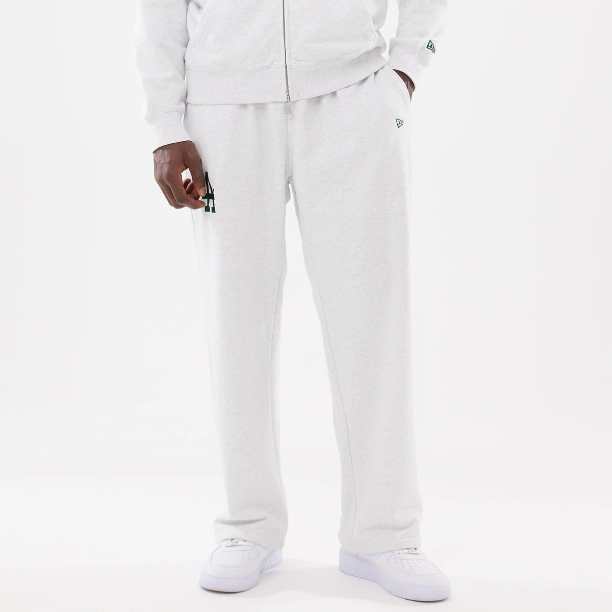 LA Dodgers MLB Comfort Grey Joggers, front view on a model with a matching zip-up top, showing the green LA logo embroidered on the left thigh and the New Era flag logo on the left pocket area.