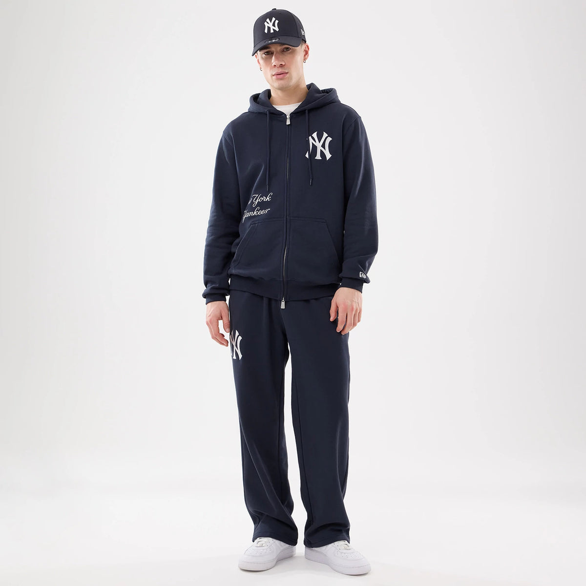 New York Yankees MLB Comfort Navy 2 Way Full Zip Hoodie, on-model view showing the navy hoodie with a white embossed Yankees logo on the chest, full zip closure, drawstring hood, and matching navy pants with a similar logo on the left leg.