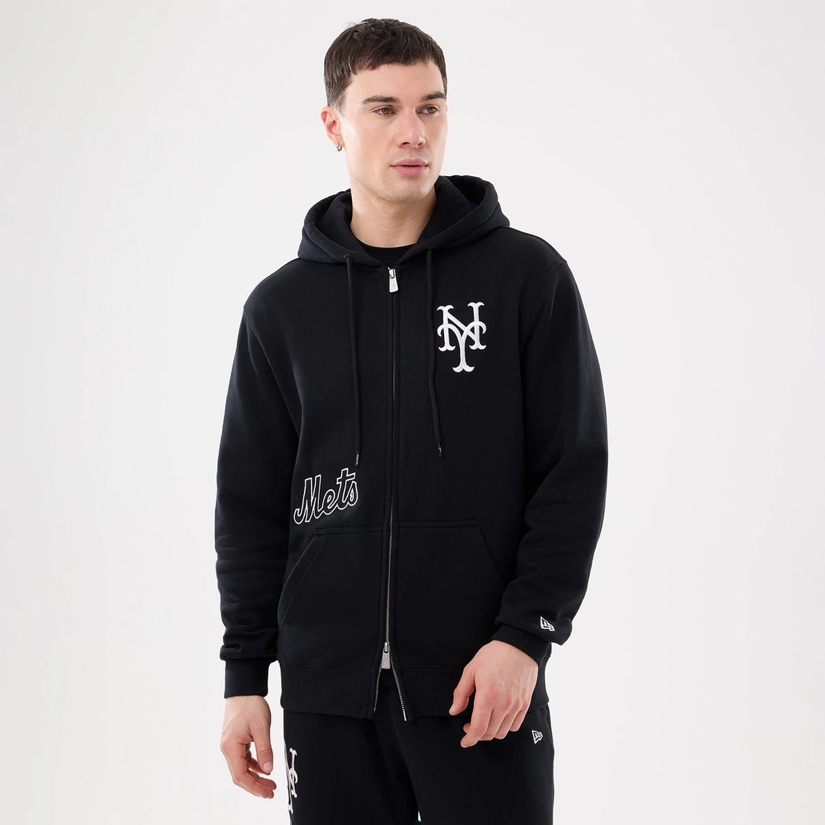 New York Mets MLB Comfort Black 2 Way Full Zip Hoodie, on-model view showing the black hoodie with a white embroidered New York Mets logo on the left chest, Mets lettering above the pocket, and a raised New Era logo on the sleeve cuff.