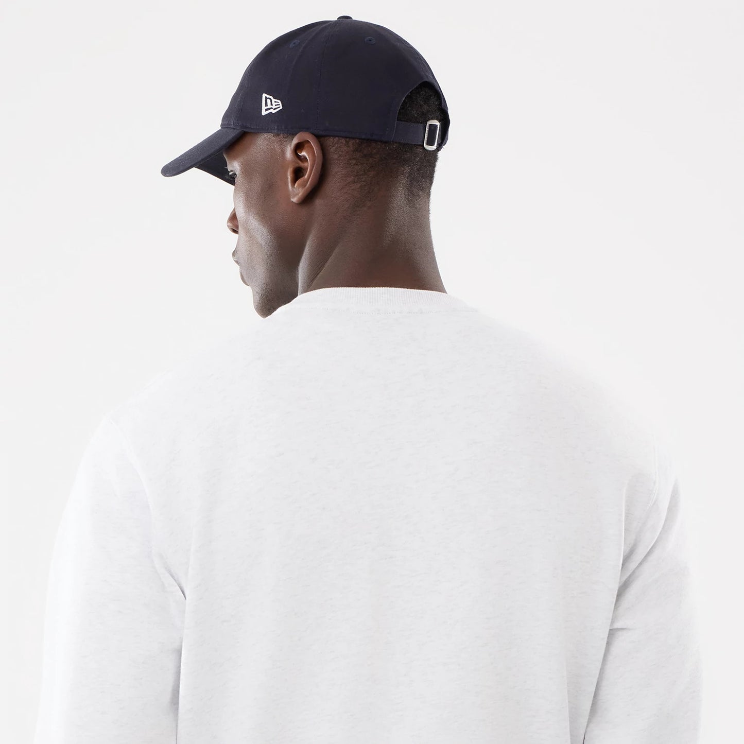 New York Yankees MLB Retro White Oversized Crew Neck Sweater, rear view on a model with a navy cap, showing the New Era flag logo on the left side and a white adjustable strap at the back.