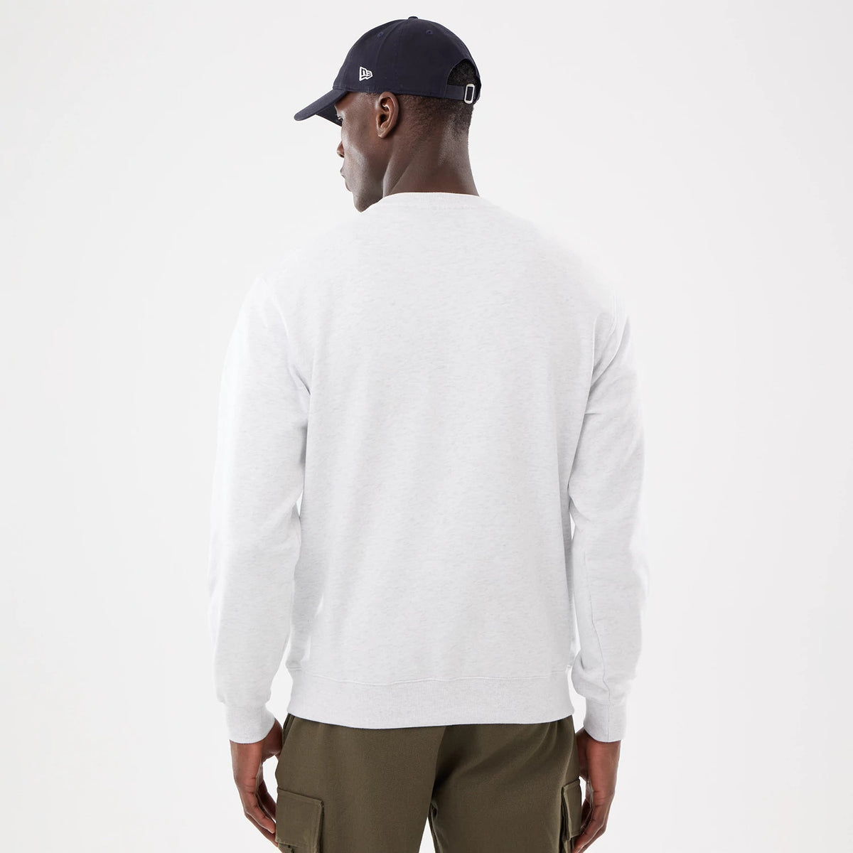 New York Yankees MLB Retro White Oversized Crew Neck Sweater, back view on a model wearing a dark cap, showing the plain white fabric with ribbed cuffs and hem, paired with olive cargo trousers for a casual look.