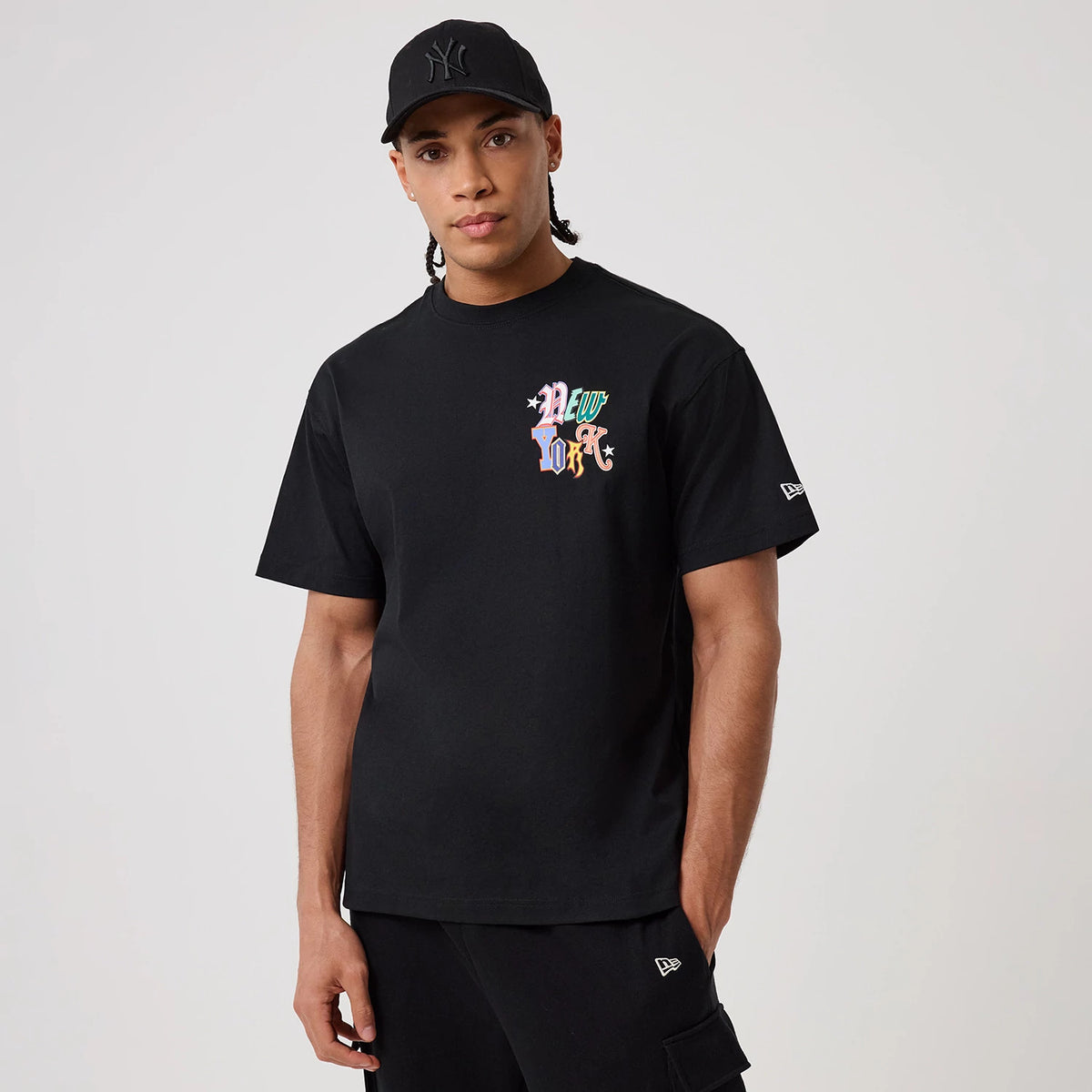 New York Yankees MLB Word Art Black T-Shirt, on-model view showing the black T-shirt with multicoloured "New York" text on the chest and a small embroidered New Era logo on the left sleeve.