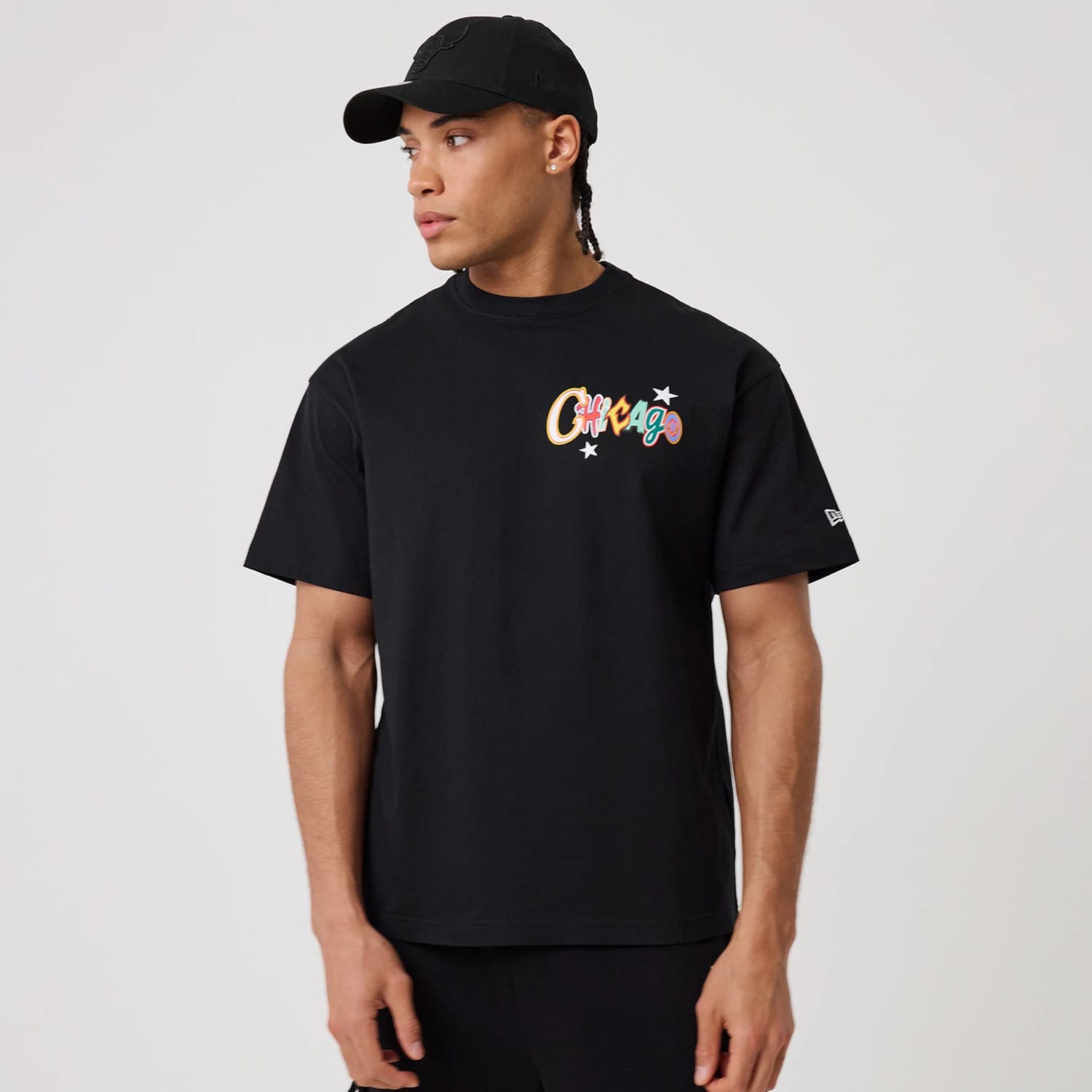 Chicago Bulls MLB Word Art Black T-Shirt, on-model view showing a black tee with 'Chicago' in colourful text and stars on the left chest, a raised New Era logo near the short sleeve edge, worn with a matching black cap.