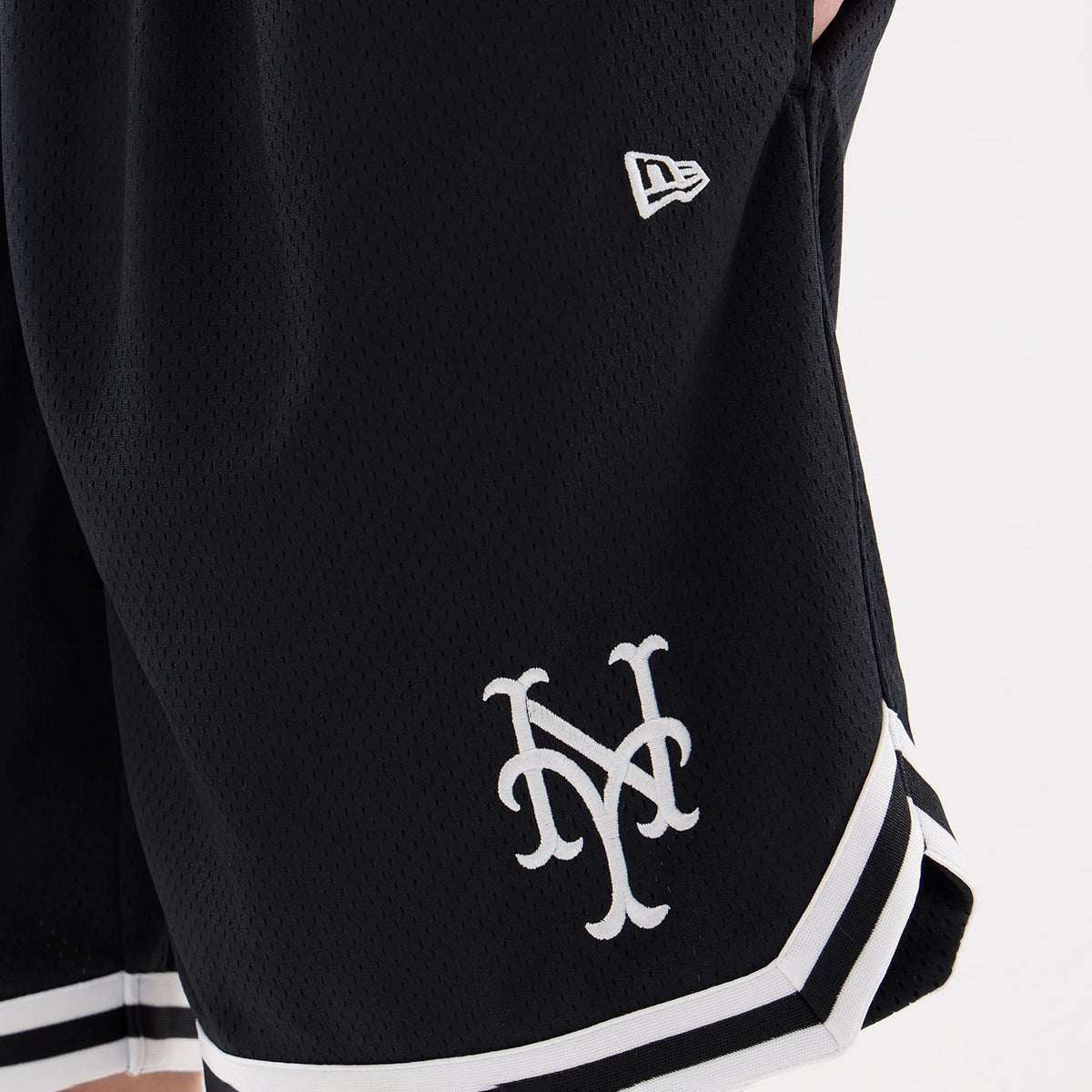 New York Mets MLB Comfort Navy Oversized Shorts, three-quarter view showing the white raised New York Mets logo near the hem with a smaller white raised New Era logo above, accented by black and white striped trim.