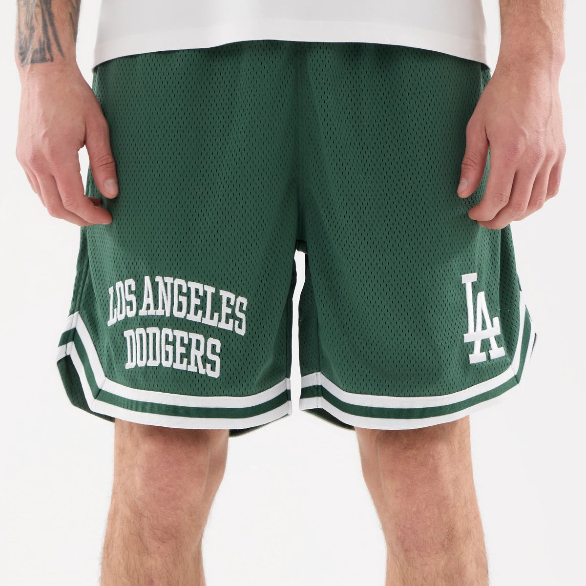 LA Dodgers MLB Comfort Dark Green Oversized Shorts, front view showing the dark green fabric with white "LOS ANGELES DODGERS" text on the left leg, and a white "LA" logo on the right leg above double white stripe trim.