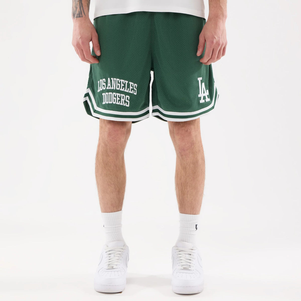 LA Dodgers MLB Comfort Dark Green Oversized Shorts, front view showing the bold Los Angeles Dodgers text on the left leg, LA initials on the right leg, and white striped detailing around the hem above the knee.