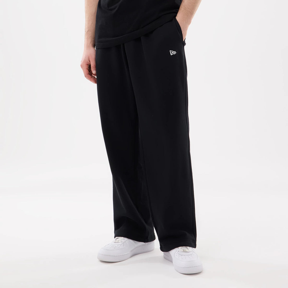 New Era Black Straight Legged Joggers, front view on a model wearing a black T-shirt and white trainers, with the New Era flag logo embroidered on the left pocket above the straight black legs.