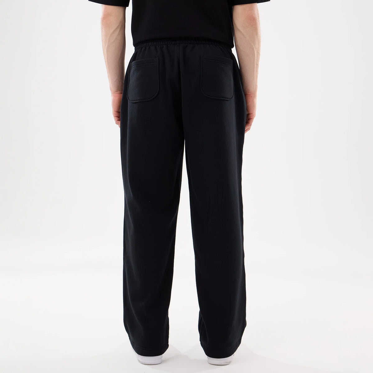 New Era Black Straight Legged Joggers, rear view on a model with two large back pockets, an elasticated waistband, and straight-leg cut falling to white sneakers, paired with a black t-shirt.