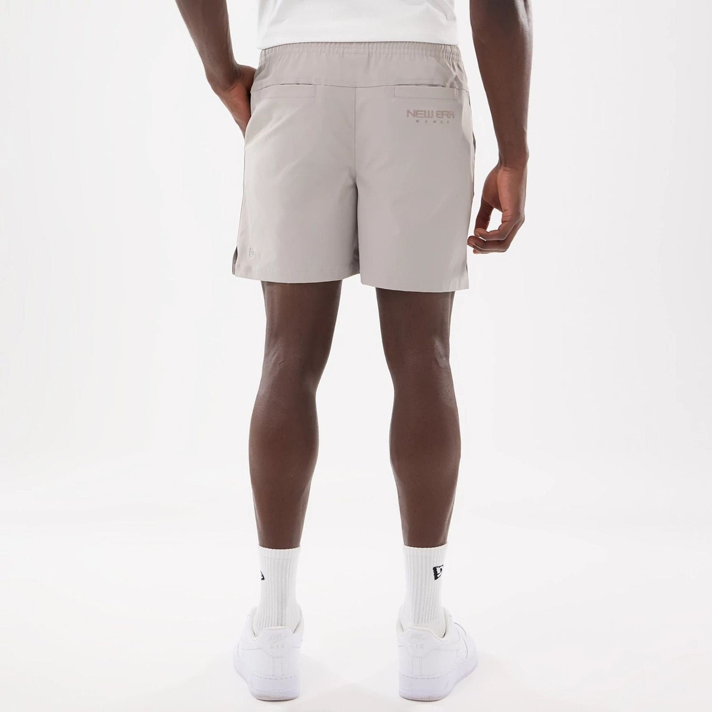 New Era NEC Logo Beige Oversized Shorts, rear view showing the relaxed fit with an elastic waistband, pockets on either side, a debossed New Era logo on the right pocket, and a small slit at the hem.