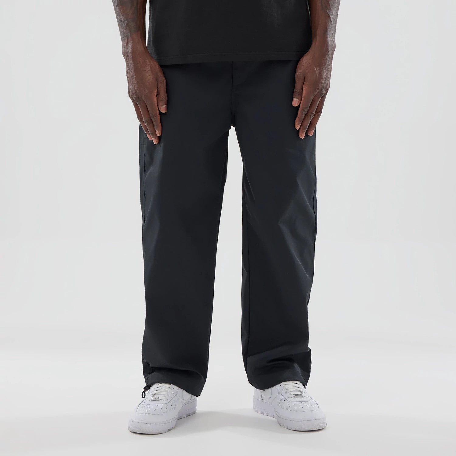 New Era NEC Logo Black Straight Leg Joggers, front view on a model wearing white trainers and a black top, highlighting the relaxed fit and simple waistband with drawstring cuffs at the ankles.